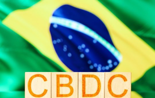 Wooden blocks emblazoned with the letters CBDC against a backdrop of the Brazilian flag.